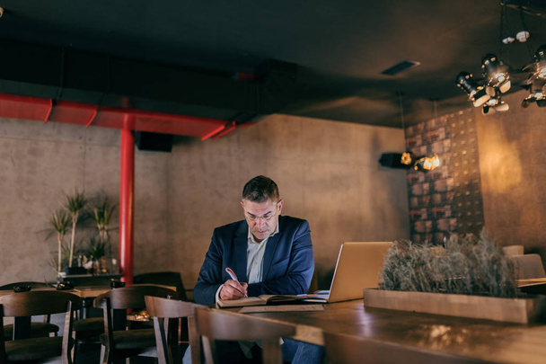 Biznesmenów w średnim wieku ubrany, smart casual wypełnienie agendy siedząc w kawiarni. Na laptopie tabeli. - Zdjęcie, obraz
