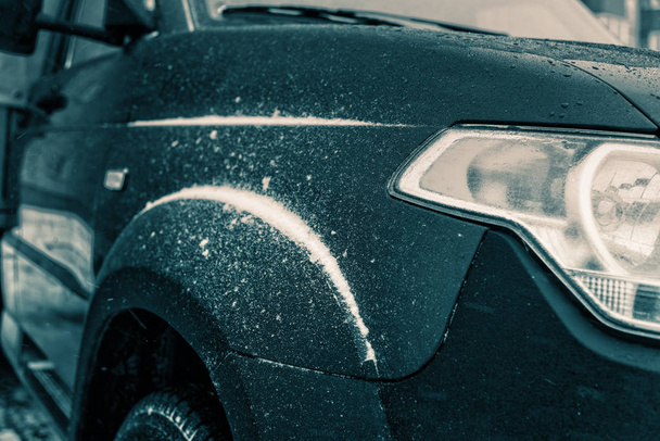 Espejo retrovisor en un coche cubierto de nieve, de pie en el estacionamiento cerca de la casa en una mañana fría, el sol brilla en la cámara. Primer plano de los neumáticos del coche en invierno en la carretera cubierta de nieve
. - Foto, imagen