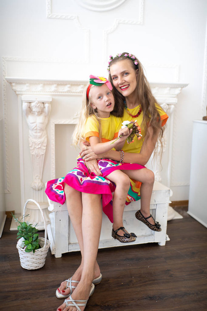 Style summer family look. Mom and daughter love. Take care of the child and ensure a happy childhood. Fun holidays. Bright yellow pink dress and floral decorations. White professional studio banner - Photo, Image