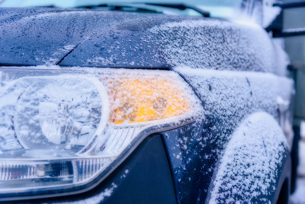 Taustapeili lumen peittämässä autossa, seisoo pysäköintialueella lähellä taloa kylmänä aamuna, aurinko paistaa kameraan. Lähikuva auton renkaat talvella tiellä peitetty lumella
. - Valokuva, kuva