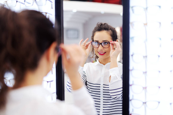 Magnifique femme caucasienne avec les cheveux bouclés essayer des lunettes chez opticien
. - Photo, image