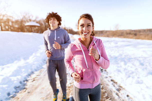 Счастливые белые друзья в спортивной одежде, бегущие на свежем воздухе. Зима, снег повсюду. Понятие здорового образа жизни
. - Фото, изображение