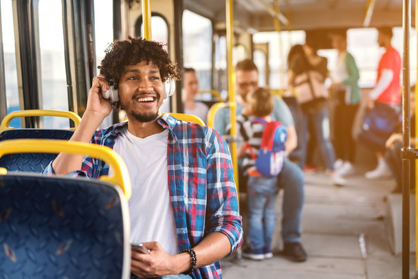 young happy man sitting in a bus seat listening to music through headset  - Photo, Image
