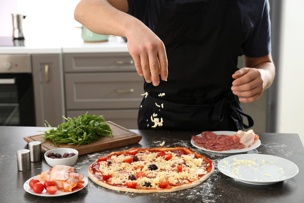 Молодий чоловік готує смачну піцу за столом
 - Фото, зображення