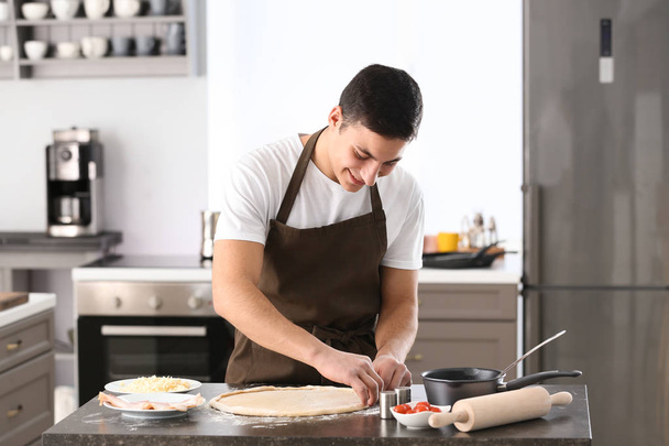 Young man preparing dough for pizza at table - Фото, зображення