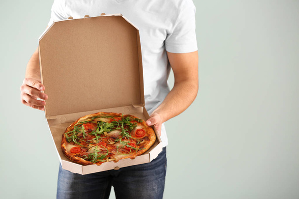 Young man holding box with tasty pizza on light background - 写真・画像
