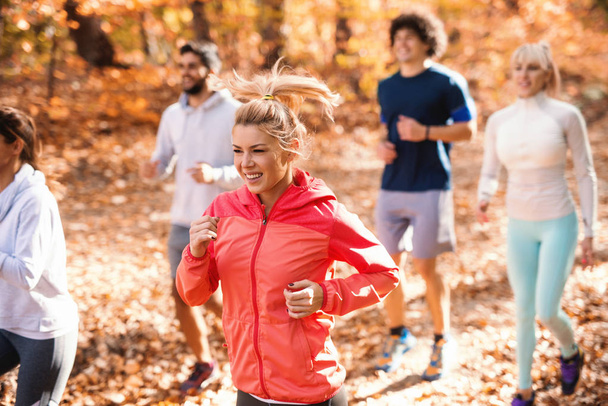 Μικρή ομάδα ανθρώπων που τρέχει στο δάσος το φθινόπωρο. Επιλεκτική εστίαση στην ξανθιά γυναίκα. - Φωτογραφία, εικόνα