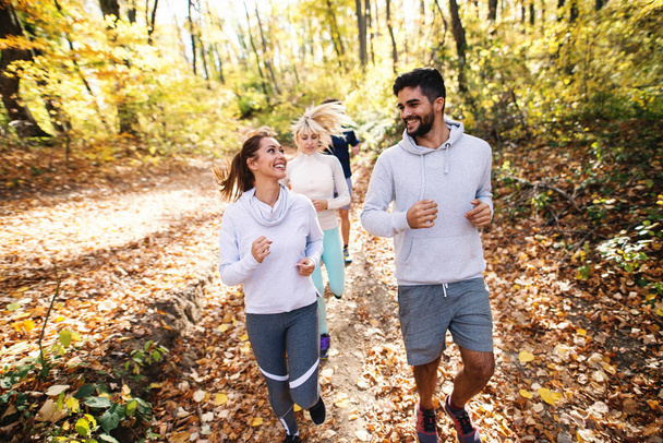 Small group of people running in woods in the autumn. In foreground couple smiling at each other. - 写真・画像