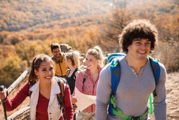 Happy small group of hikers walking in the row in the autumn. Selective focus on blonde woman. - Photo, Image