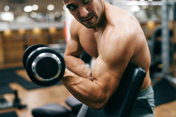 Közelkép a félmeztelen izmos ember gyakorolja a bicepsz, súlyzó. - Fotó, kép