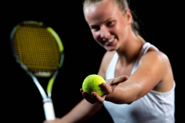 Young woman on a tennis practice. Beginner player holding a racket, learning basic skills. Portrait on black background. - Photo, image