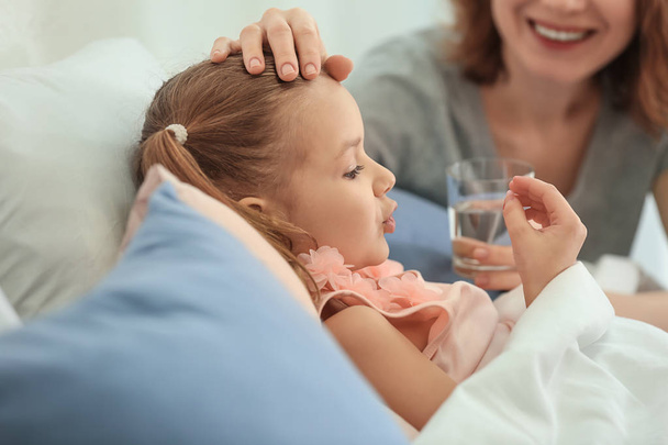 Jeune femme donnant pilule pour sa fille malade au lit
 - Photo, image