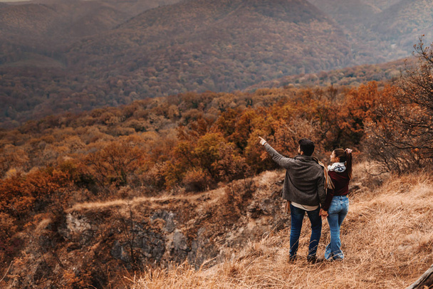 Couple holding hands and enjoying nature. Man pointing at mountain. Backs turned, autumn time. - Photo, Image