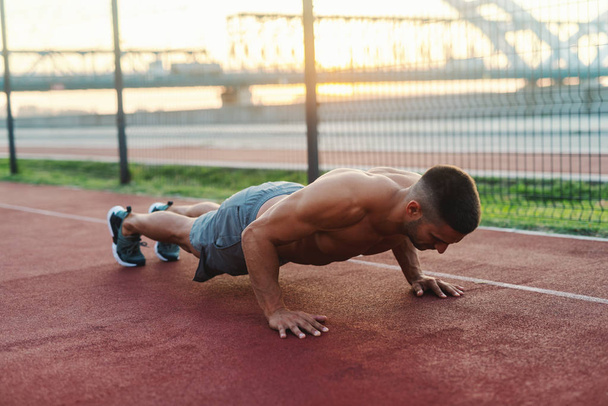 Shirtless strong dedicated muscular man doing push ups on the court in the morning. - Photo, Image