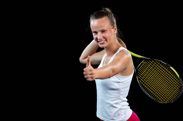 Female athlete posing with tennis racket against black background - Foto, imagen