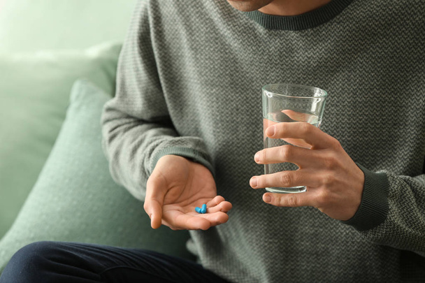 Молодий чоловік з таблетками і склянкою води в приміщенні, крупним планом
 - Фото, зображення