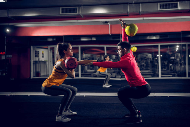 Paar doelen. Fit jonge paar trainen in een sportschool. Doen squats terwijl gewichten in hun handen. - Foto, afbeelding