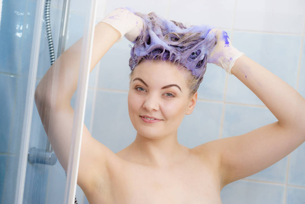 Woman applying coloring shampoo on her hair. Female having purple washing product. Toning blonde color at home. - Fotoğraf, Görsel