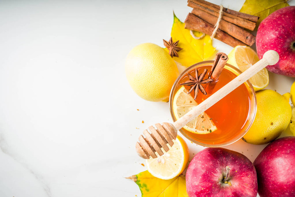 Two cups of autumn winter hot spicy tea with red apples, lemons, cinnamon, anise, honey, White marble background copy space - 写真・画像