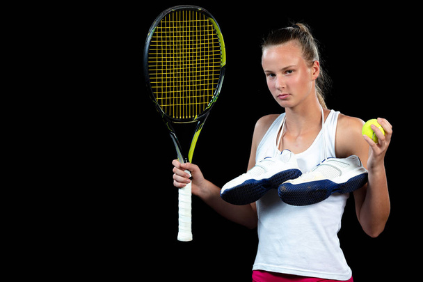 Young woman on a tennis practice. Beginner player holding a racket, learning basic skills. Portrait on black background. - Photo, image