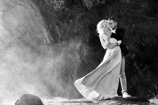 Szerelmes pár áll a fröccsenő víz ellen a naplementét. Egy ember hugs egy nőt egy szép ruha. Szeretet az a szem - Fotó, kép