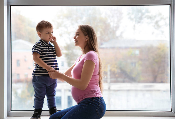 Giovane donna incinta con il suo piccolo figlio carino vicino alla finestra
 - Foto, immagini