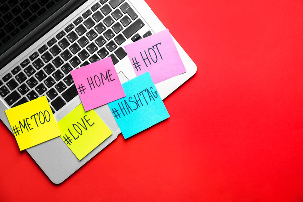 Laptop en papier vellen met populaire hashtags op kleur achtergrond - Foto, afbeelding