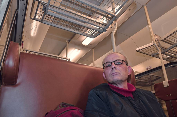 Hombre de mediana edad mirando por la ventana del tren. Pasajero durante el viaje en tren expreso de alta velocidad en Europa. Anciano viajando en tren por la noche
.  - Foto, imagen
