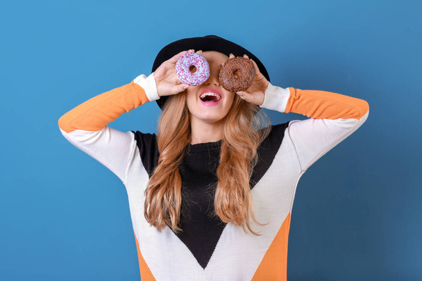 Mooie jonge vrouw met lekkere donuts op kleur achtergrond - Foto, afbeelding