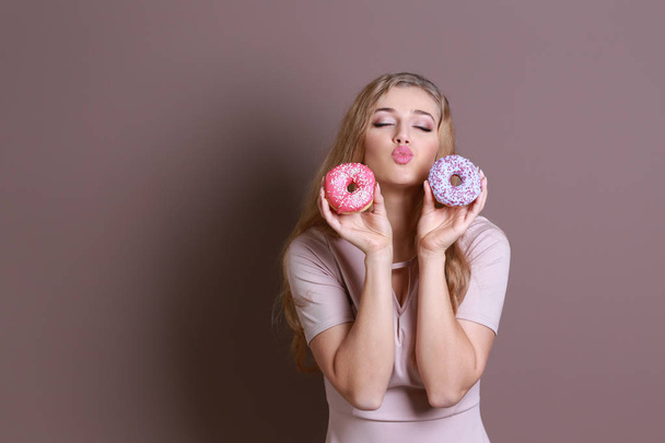 Funny young woman with tasty donuts on color background - Fotoğraf, Görsel