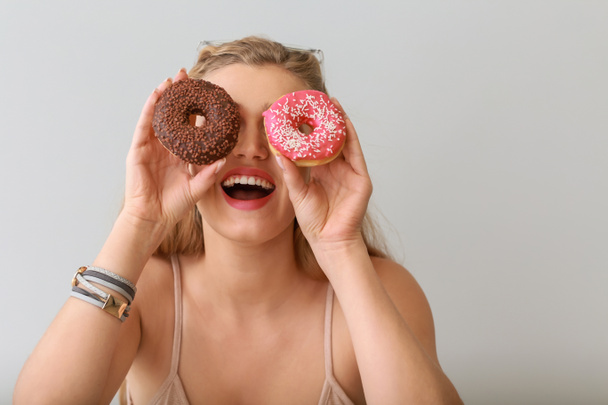Lezzetli donuts ışık arka plan üzerinde olan komik kadın - Fotoğraf, Görsel