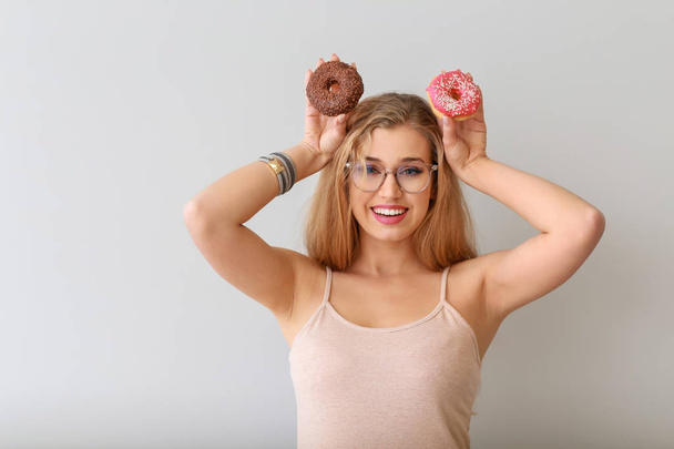 Mujer joven divertida con rosquillas sabrosas sobre fondo claro
 - Foto, imagen