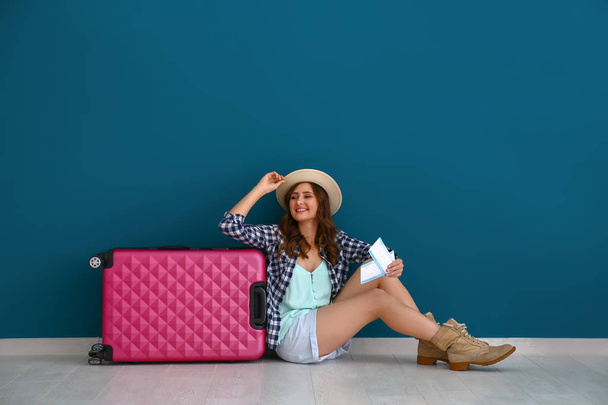Female tourist with luggage sitting near color wall - Photo, Image