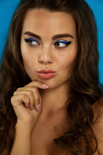 Portrait of a beautiful brunette girl with fashion make-up with black and blue eyeliner on blue background - Photo, image
