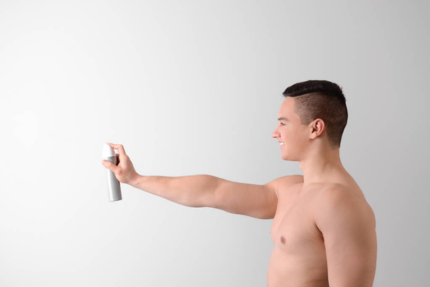 Młody człowiek z dezodorant na jasnym tle - Zdjęcie, obraz