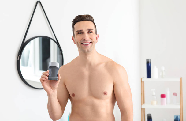 Handsome young man with deodorant in bathroom - Photo, Image