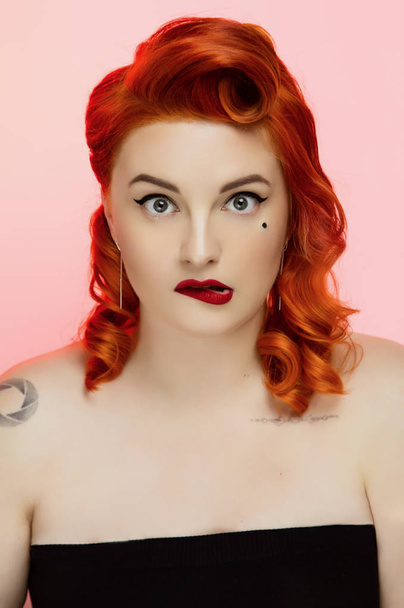 Portret van een mooie rode-haren-meisje met pin-up make up en haar in de studio, kleur achtergrond, emoties - Foto, afbeelding