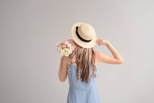 Beautiful young woman with bouquet of flowers on grey background, back view - Photo, image