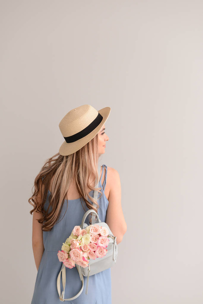 Beautiful young woman with bouquet of flowers and backpack on grey background - Foto, imagen
