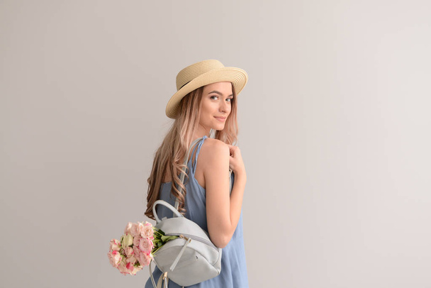 Gyönyörű fiatal nő, csokor virágot és a hátizsák a szürke háttér - Fotó, kép