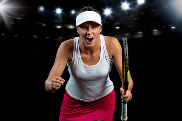 schöne Tennisspielerin mit einem Schläger auf dunklem Hintergrund mit Lichtern, die einen makellosen Sieg feiern - Foto, Bild