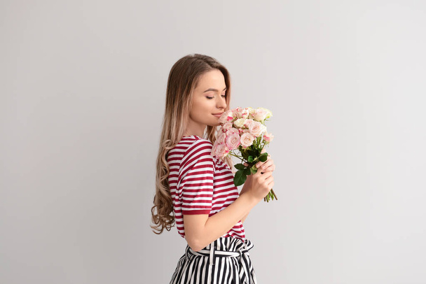 Όμορφη νεαρή γυναίκα με το μπουκέτο λουλούδια σε γκρίζο φόντο - Φωτογραφία, εικόνα