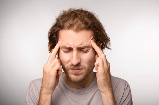 Young man suffering from headache on light background - Photo, Image