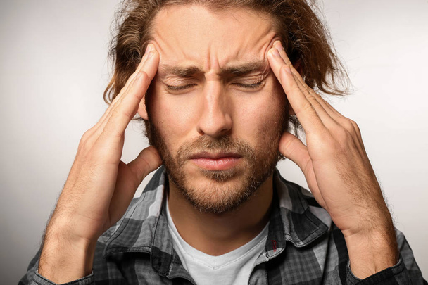 Young man suffering from headache on light background - Foto, afbeelding