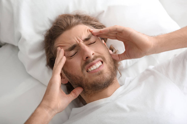 Junger Mann leidet unter Kopfschmerzen im Schlafzimmer - Foto, Bild