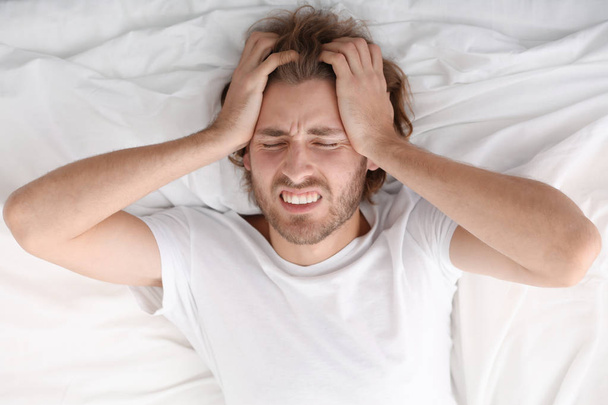 Молодой человек страдает от головной боли в спальне
 - Фото, изображение