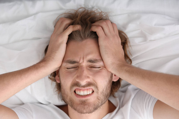Mladý muž trpí bolestí hlavy v ložnici - Fotografie, Obrázek