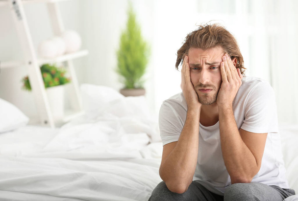 Jonge man die lijden aan hoofdpijn in slaapkamer - Foto, afbeelding