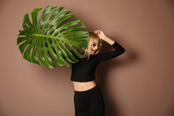 Portret van mooie vrouw met groene tropische blad op kleur achtergrond - Foto, afbeelding
