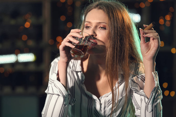 Young woman drinking alcohol and smoking cigar in bar - Photo, Image